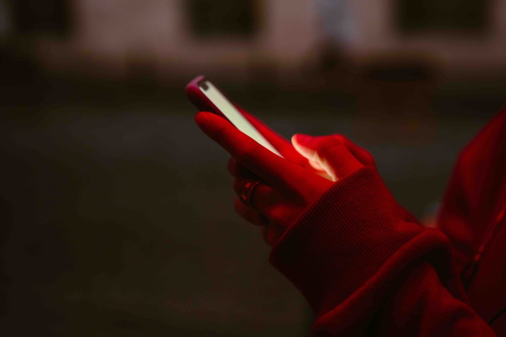 A person wearing a red hoodie uses a smartphone to enter a contest, lit by the glow of the screen.